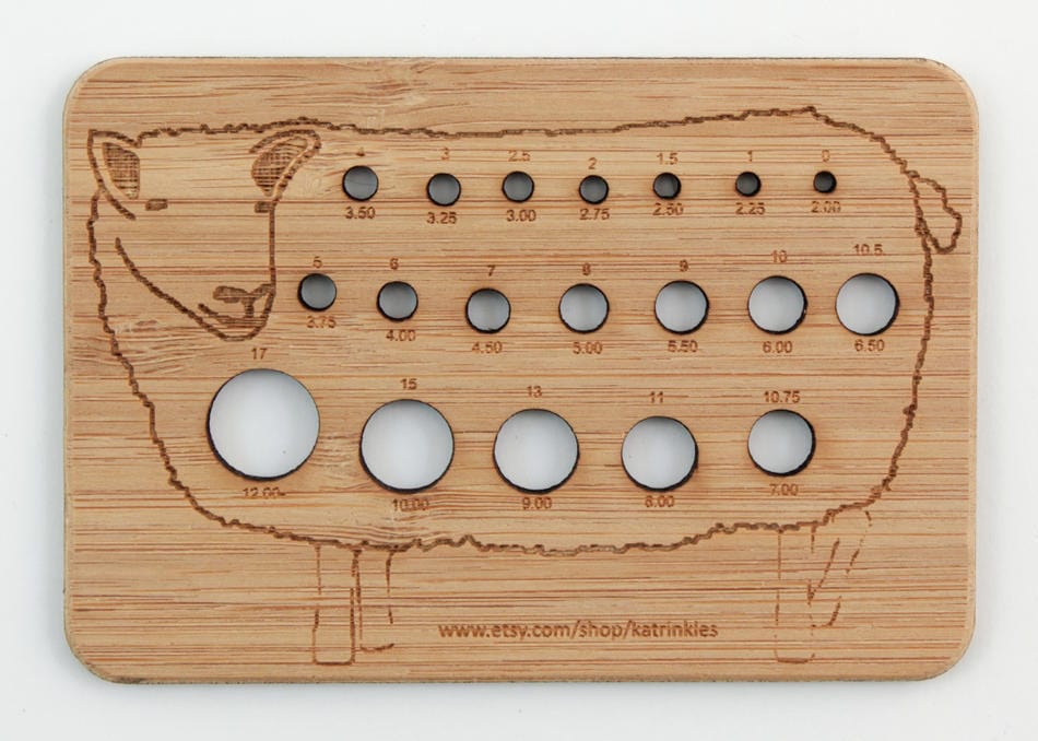 The Katrinkles Animal Needle Gauge is a wooden sheep-shaped tool with labeled holes for measuring knitting needle sizes, featuring the website www.etsy.com/shop/katrinkles engraved at the bottom.