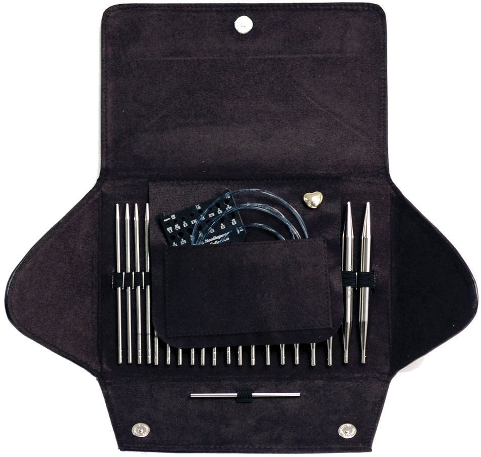 A black fabric case opens to reveal the Skacel Addi-Click Interchangeable Bamboo Needle Set with bamboo needle tips, cables, a needle gauge, and accessories neatly organized in separate compartments.